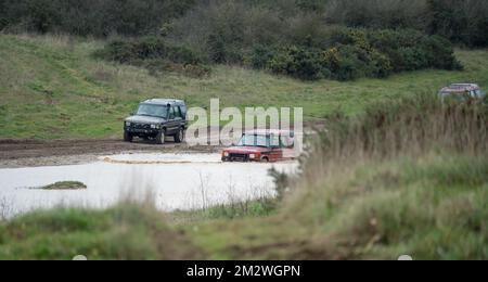 two land rover discovery 4x4 off-road vehicles being driven through deep water and mud in open countryside, Wiltshire UK Stock Photo
