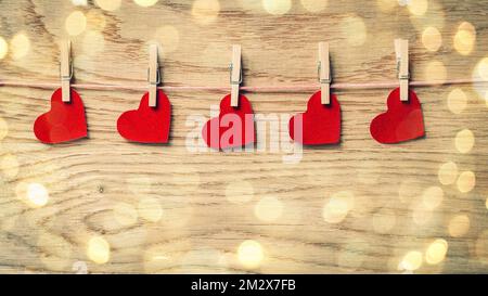 red hearts on clothespins on wooden background. beautiful bokeh effect from a garland. Stock Photo