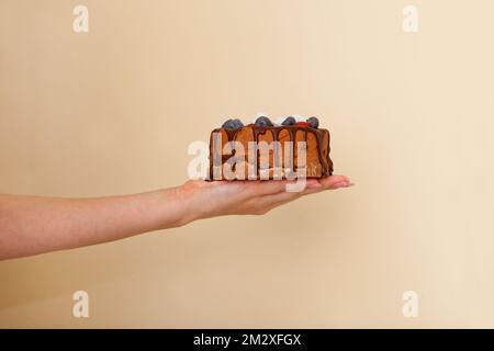 chocolate cake on woman hand. small pie with berries. Ladys Hand holding tart over beige background Stock Photo