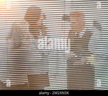 through the blinds. office staff discuss working documents. communication of partners against the background of sunset Stock Photo