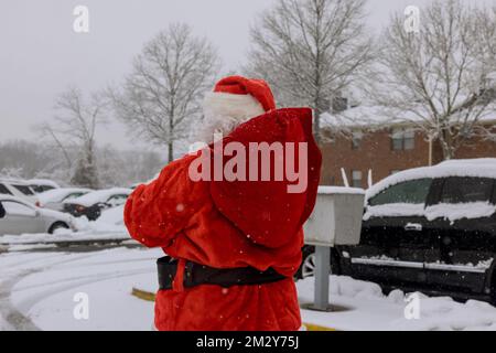 An Santa Claus walking holding red bag full of presents for children is displayed on white covered in snow. Stock Photo