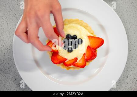 Close up of hand decorating strawberry tart with blueberries Stock Photo