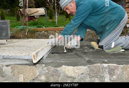The bricklayer levels the floor using a spirit level and sand before laying tiles Stock Photo