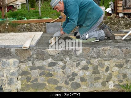 The bricklayer levels the floor using a spirit level and sand before laying tiles Stock Photo