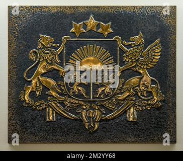 Closeup of gold color coat of arms of Latvia embossed on a relief dark metal plate. Stock Photo