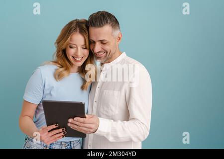White happy couple hugging and using tablet computer isolated over blue background Stock Photo