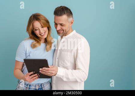 White happy couple hugging and using tablet computer isolated over blue background Stock Photo
