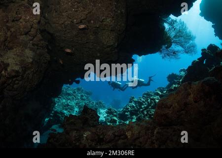 A view through the cave where two scuba divers swim along the reef.