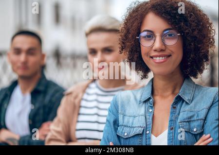 Smiling joyous woman in spectacles and her friends outdoors Stock Photo