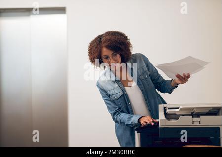 Joyous focused female secretary using the copy machine Stock Photo