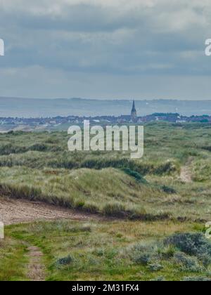 The steeple of Coatham Church and its surrounding houses seen against the Cleveland Hills and an overcast sky from rugged, grass covered sand dunes. Stock Photo