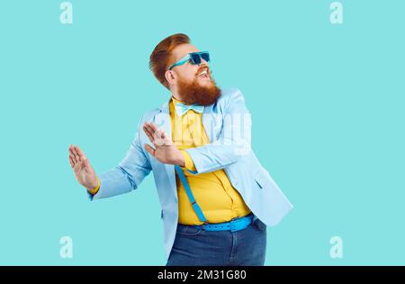 Cool cheerful stylish fat man rejoices and funny dances isolated on light blue background. Stock Photo