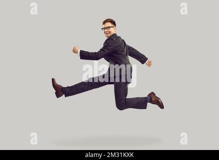 Young Caucasian man jumping and smiling posing in pose of runner dressed in business style Stock Photo