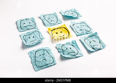A sad face watching smiling faces from afar. Happy and sad faces drawn on blue stickers. Concepts of exclusion, difference, jealousy. High quality pho Stock Photo