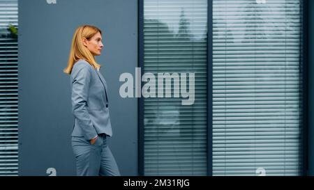 Proud confident stylish woman leader boss professional worker in formal suit walking down street against backdrop of office building successful Stock Photo