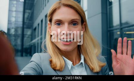 Close-up view from webcam young positive female blogger records vlog waving hello talking on video call using smartphone outdoors successful Stock Photo