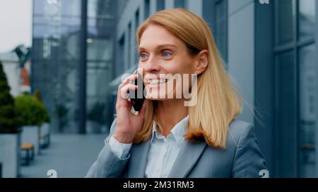 Happy enthusiastic excited woman talking on mobile phone outdoors sharing good experience with friend remotely chatting on smartphone joyful Stock Photo