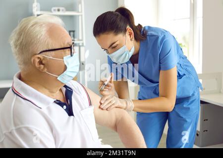 Physician in medical face mask making injection of medication to elderly man Stock Photo