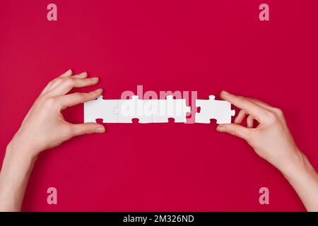 Woman holds in hand a jigsaw puzzle isolated on red or magenta background. Business solutions, success and strategy concept. Stock Photo