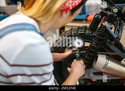 Mechanic woman checking tire air pressure of motorcycle Stock Photo