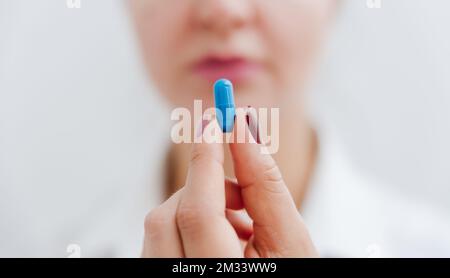 Women's hand with blue pill, vitamin, capsule. Medical insurance, medical treatment concept. Disease, sick treatment, cold season concept. Close-up vi Stock Photo