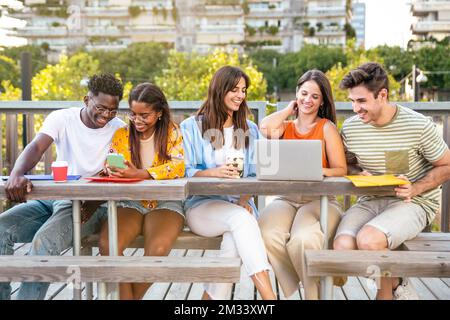 Cheerful group of university students studying for exam in the campus - Multicultural group of friends working together outdoors. Stock Photo