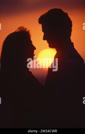 Silhouette of couple embracing with sunset/sunrise behind them Stock Photo