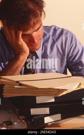 Businessman with head in hand with a pile of work to do Stock Photo