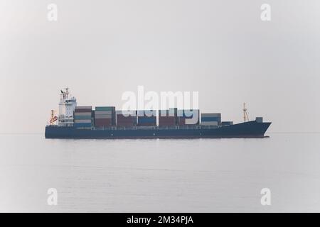 Cargo freight ship with containers and trucks sailing to industrial logistic port. Stock Photo
