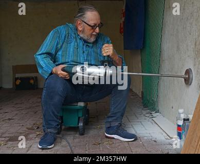 Active elderly man is drilling a hole in the wall of a garage with a jackhammer and a Rotary Hammer Core Bit Stock Photo