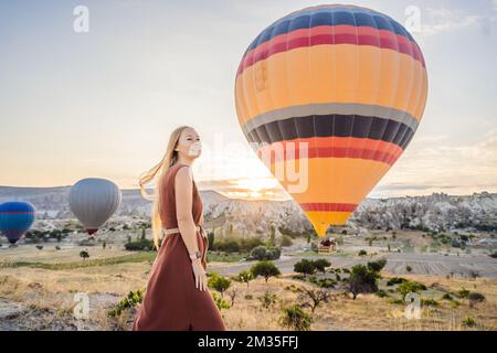 Tourist woman looking at hot air balloons in Cappadocia, Turkey. Happy Travel in Turkey concept. Woman on a mountain top enjoying wonderful view Stock Photo
