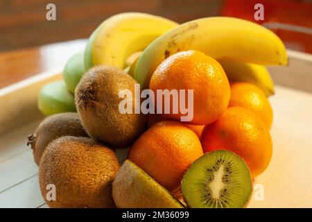 On a white wooden tray, seasonal fruit, mandarins, banana and kiwi with their distinctive orange, yellow and green colors Stock Photo