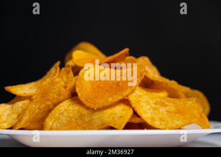 Thin crispy potato chips on a plate on a black background Stock Photo