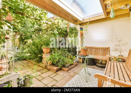 a patio with lots of plants and pots on the ground in front of a white brick wall that has been painted yellow Stock Photo