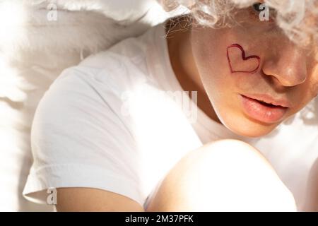 Girl dressed as an angel with wings and curly hair with a painted heart ...