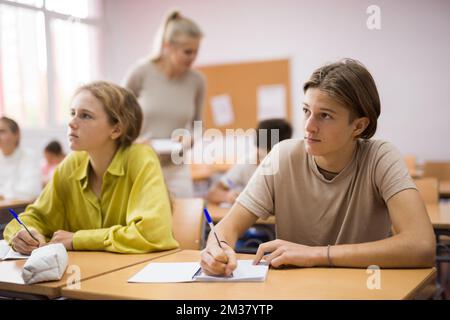Boys and girls sitting at desk in classroom full of pupils during lesson Stock Photo