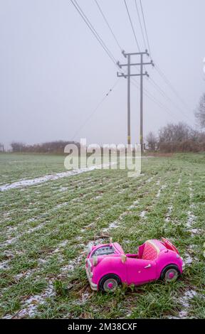 Pink retro convertible plastic toy car for 18-inch dolls by Og Girl dumped in a field on a cold, frosty day. Stock Photo