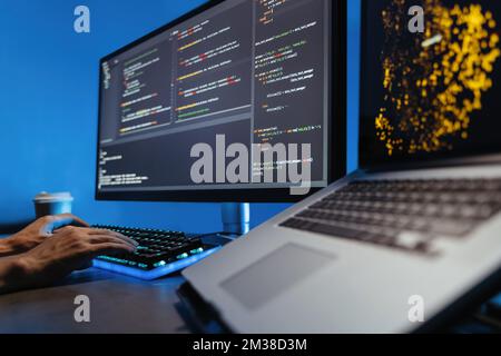 Data science concept. No face image of male hands typing on keyboard, writing html code for website, sitting at desk with pc and laptop, working on project in software development company Stock Photo