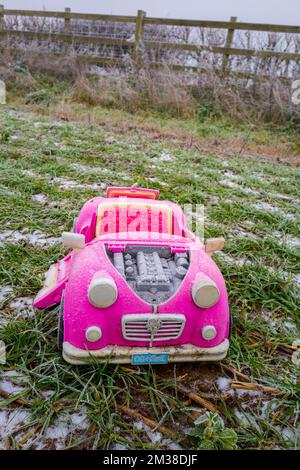 Pink retro convertible plastic toy car for 18-inch dolls by Og Girl dumped in a field on a cold, frosty day. Stock Photo