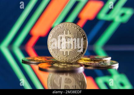 Image of bitcoins lying on mirror surface with one one standing isolated on blurred background with red and green candlesticks on digital crypto chart Stock Photo