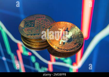 Closeup of stacked golden bitcoin cryptocurrency lying on blue digital display with candle stick graph chart representing investment stock exchange fund Stock Photo