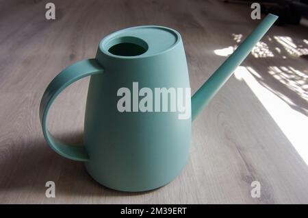 Turquoise blue watering can sitting on light wood floor with sunlight coming through the window Stock Photo