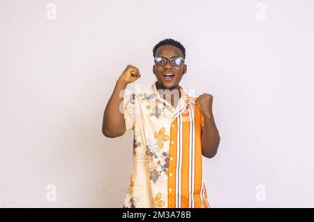 excited African American male wearing glasses isolated on a white background holding up his fists celebrating a massive win with a joyous expression o Stock Photo