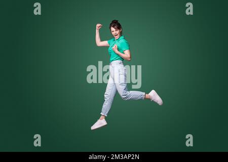 Full size profile photo of brunette lady running celebrating favorite team victory isolated on green background. Happiness, win, success. Full length. Stock Photo