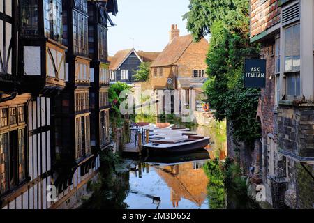Boats, period buildings and Old Weavers House with mirror reflections in the Great Stour River glowing gold soon before sunset in Canterbury, UK Stock Photo