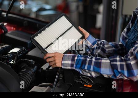 Caucasian female auto mechanic changes the engine air filter in the car. Stock Photo