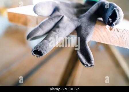 Black construction glove with rubbed fingers close-up. Holeful work gloves at a construction site on wooden scaffolding. Poor quality protective glove Stock Photo