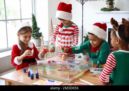 Little children in Christmas costumes pouring paints into water at workshop for Ebru painting Stock Photo