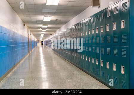 Typical, nondescript USA empty school hallway with teal green metal lockers along one side of the hallway. Stock Photo