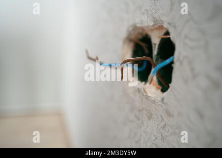 Several exposed electrical copper wires protruding from a whitewall. electrical wires and connector installed in plasterboard drywall for gypsum walls Stock Photo
